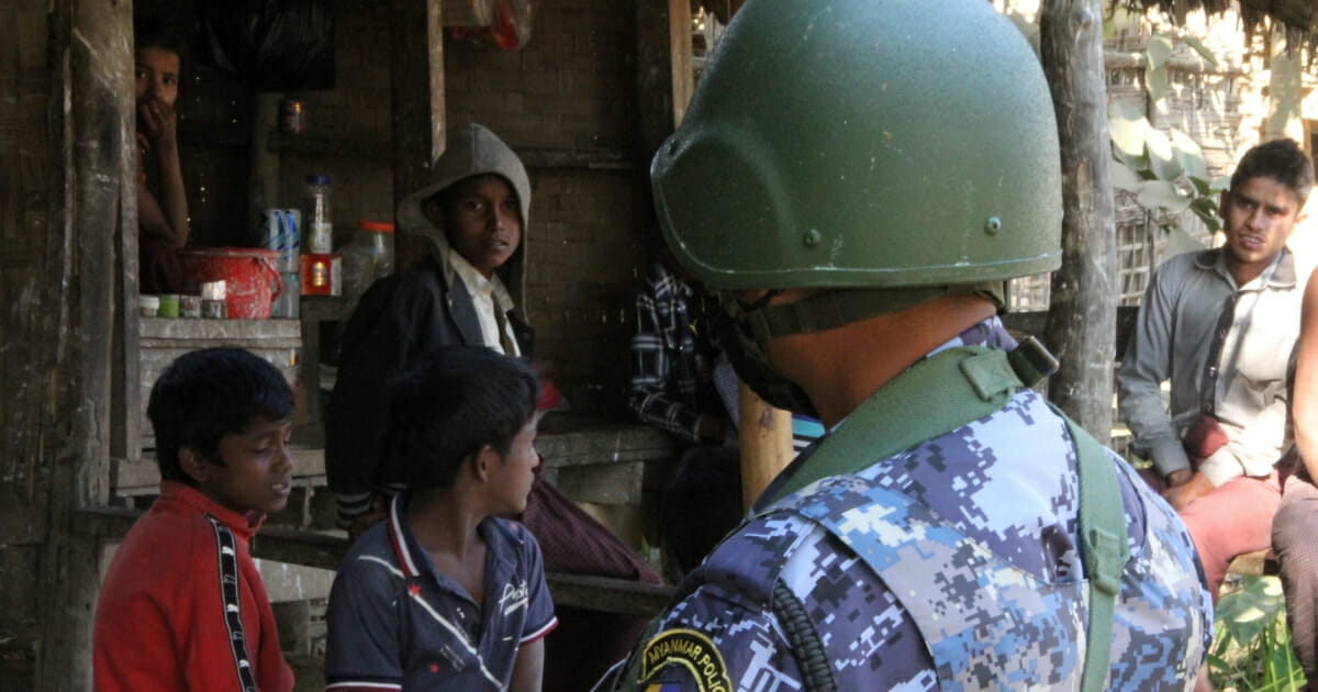 A Myanmar border guard policeman stand near a group of Rohingya Muslims in front of a small store in a village.
