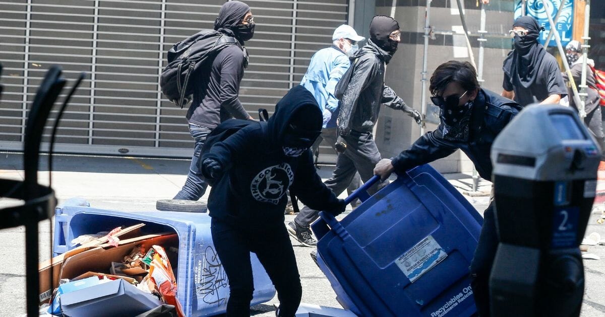 Antifa militants use fencing and trash cans to protect themselves from the smoke bombs shot at them and counter protesters by the police, on Aug. 5, 2018, in downtown Berkeley, California.