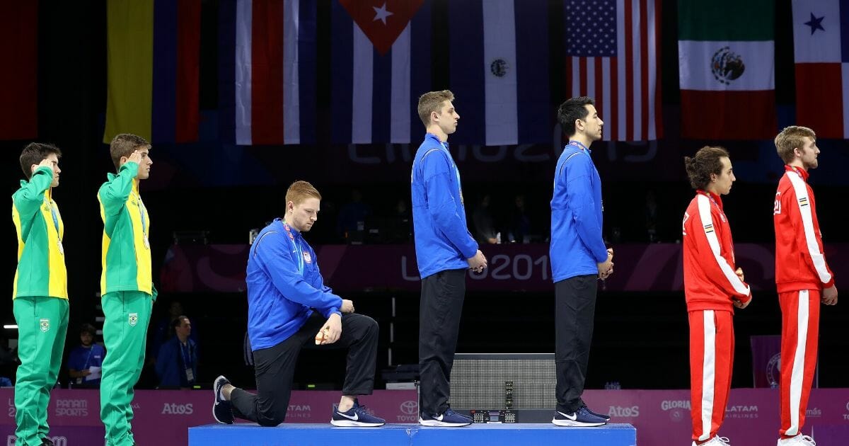 Gold medalist Race Imboden of the United States takes a knee during the national anthem ceremony on the podium of fencing men's foil team gold medal match match on day 14 of Lima 2019 Pan American Games at Fencing Pavilion of Lima Convention Center on Aug. 9, 2019, in Lima, Peru.