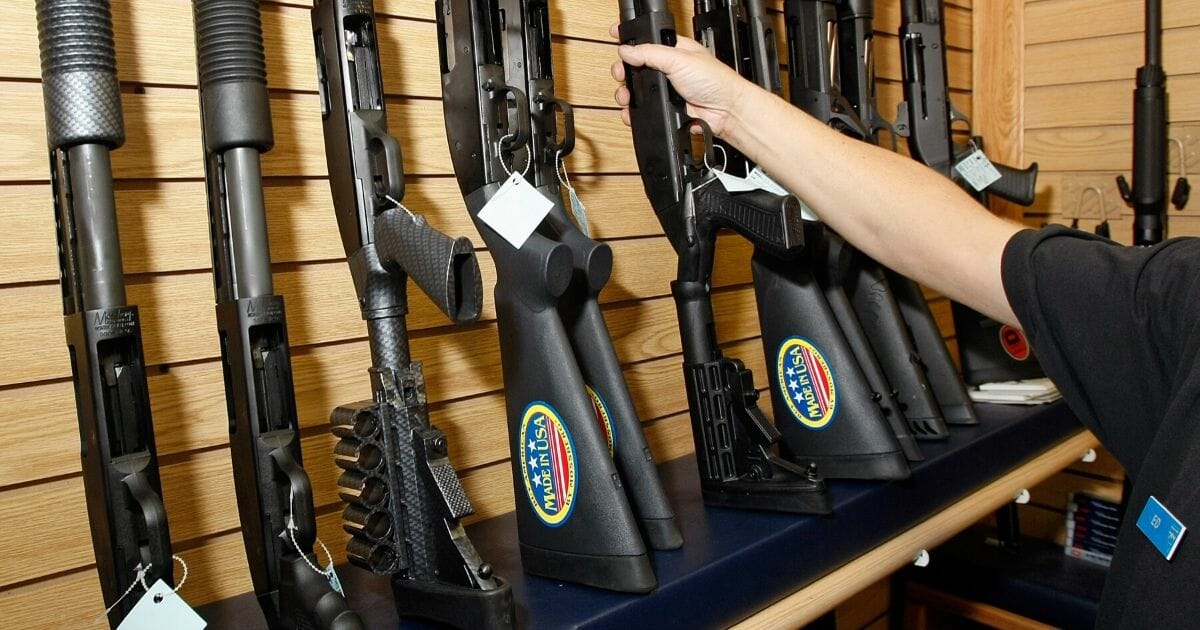 A hand reaches for a rifle on a gun store rack.