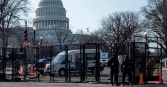 Police and National Guard troops stand at a fence outside the Capitol