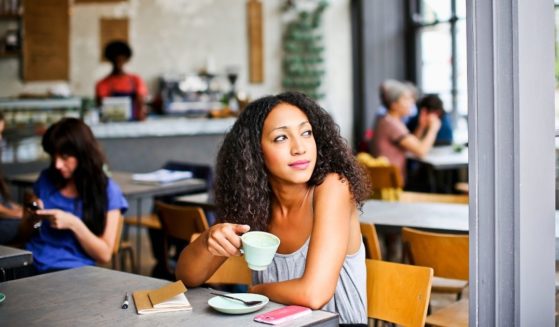 A California cafe is making waves with their take on customers who wear masks and talk about their vaccines. The above stock photo shows a woman in a cafe.