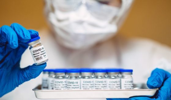 The above stock photo shows a health care professional in protective gloves and work wear holding and organizing a tray of COVID-19 vaccine vials.