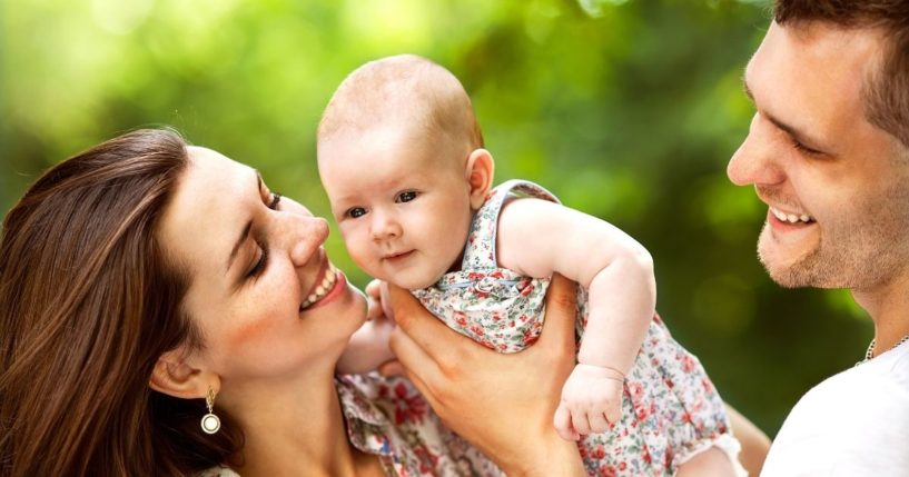 Parents play with their baby in a park.