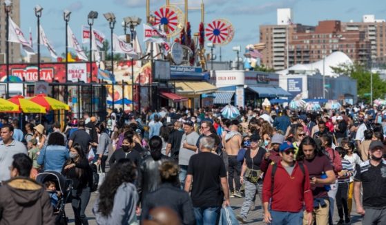 People with and without masks walk on a crowded boardwalk at Coney Island in the Brooklyn borough of New York on Memorial Day.