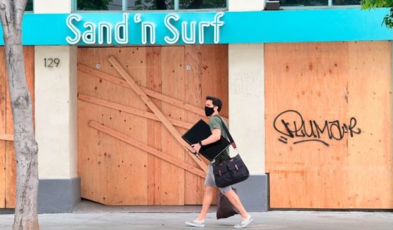 A man walks past a boarded-up Sand 'n Surf shop as many businesses were closed around the Third Street Promenade shopping district in Santa Monica, California, on June 26, 2020.