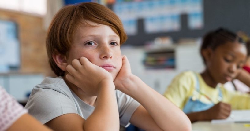 A boy looks tired and bored as he sits at his desk in a classroom.