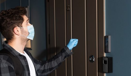 A masked man is pictured knocking on someone's front door.