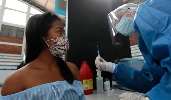 A health worker shows a syringe with a dose of the Pfizer coronavirus vaccine to a woman before administering the shot at Universidad Catolica in Quito, Ecuador, on Friday.