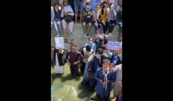 People stand in sewage outside the airport in Kabul, Afghanistan, holding up citizenship papers, hoping to be let into the airport.