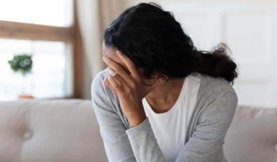 A stock photo shows a woman sitting with her face in her hand, looking sad.