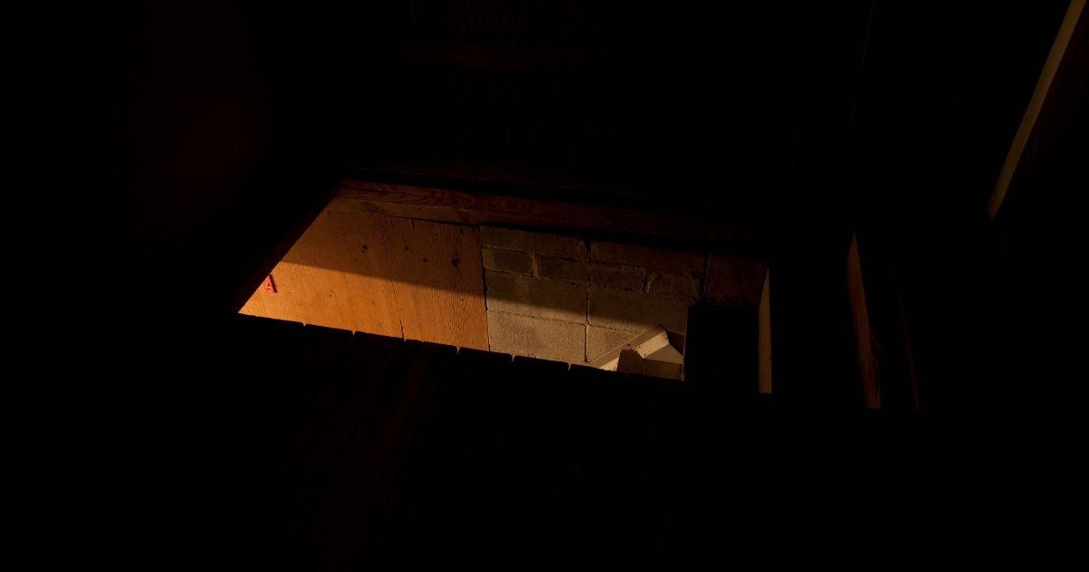 A dark attic room is seen with light coming in through the entrance.