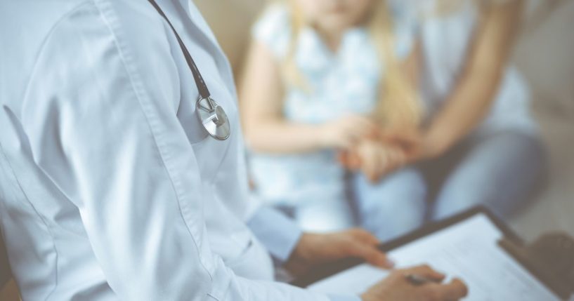 A pediatrician uses a clipboard while examining a little girl with her mother.