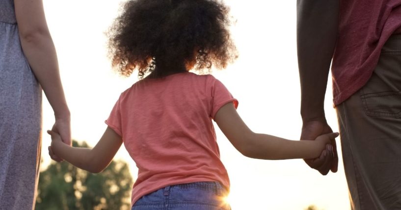 Parents hold their daughter's hands in this stock image.