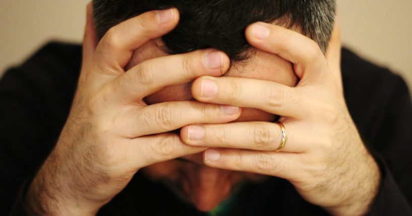 A man, presumably fed up with President Joe Biden, holds his head in his hands in the above stock image.