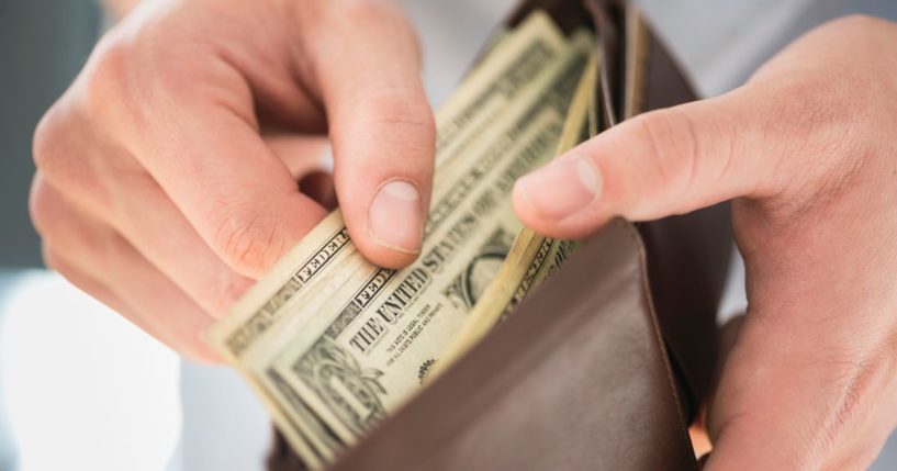 A man takes money out of a wallet in the above stock image.