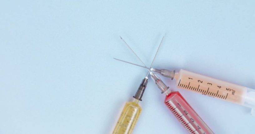 Syringes with different medicines in yellow, red, orange and transparent colors lie on a blue background. Published on January 27, 2021 (Unknown/Via Unsplash)