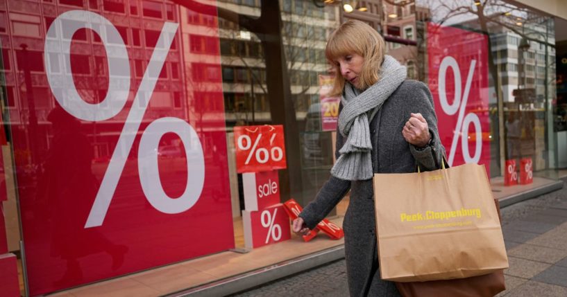 A woman walks with purchases past a store