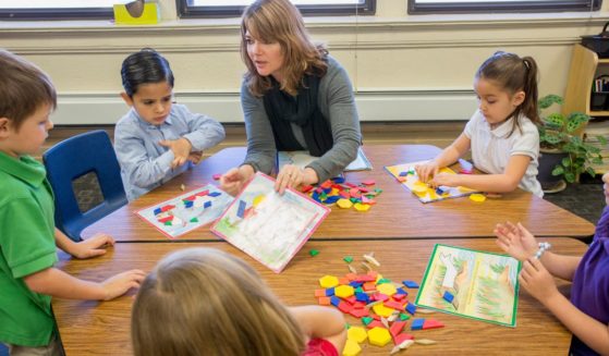 A teacher is pictured helping young students with a project in a classroom.