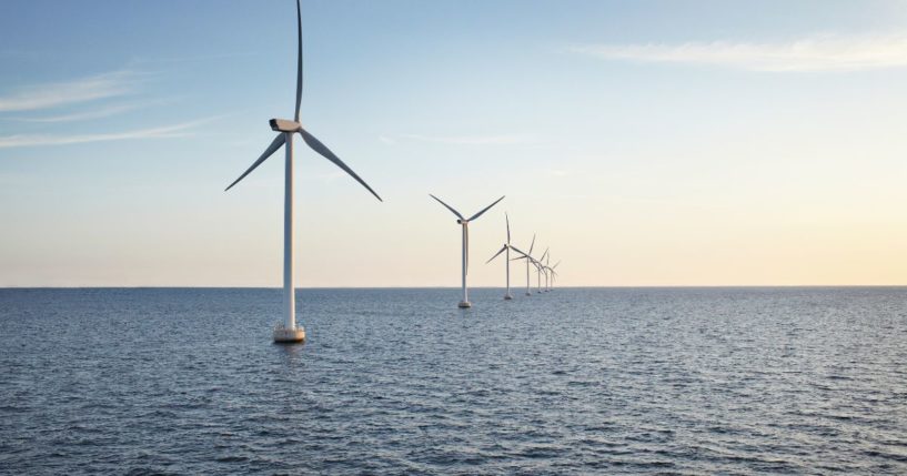 A row of wind turbines are shown in the sea at sunset.