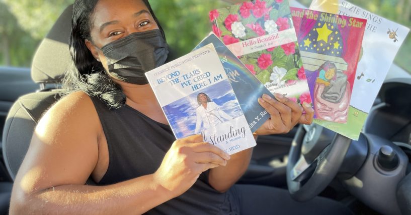 Tomika Reid holds up books that she has authored in her car that she uses to be a Lyft driver in Princeton, New Jersey.