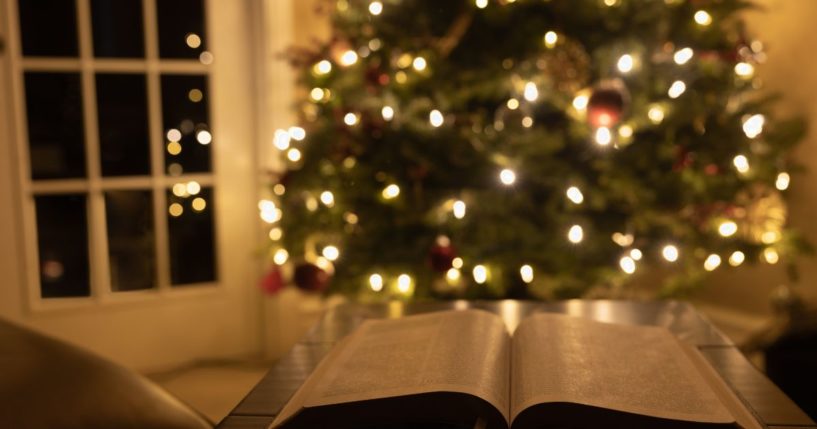 A Bible lays open in front of a Christmas tree in this stock image.