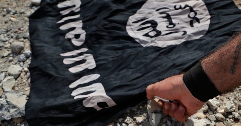 A fighter from the Christian Syriac militia that battles the Islamic State group burns an IS flag in a file photo from July of 2017.