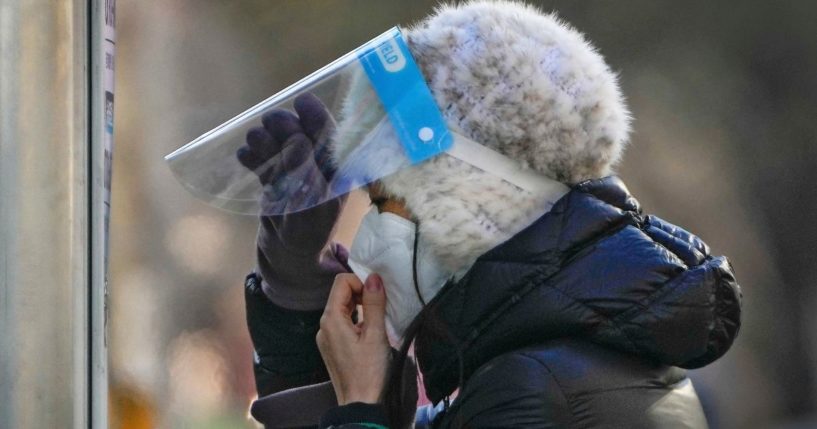 A woman wearing a face mask and face shield gets ready for her routine COVID-19 throat swab at a coronavirus testing site in Beijing, on Wednesday.