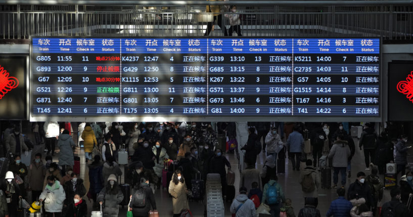 Travelers walk under a train departure board in the West Railway Station of Beijing China, on Sunday.