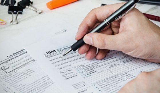 A man's hand holds a pen to an IRS 1040 form.