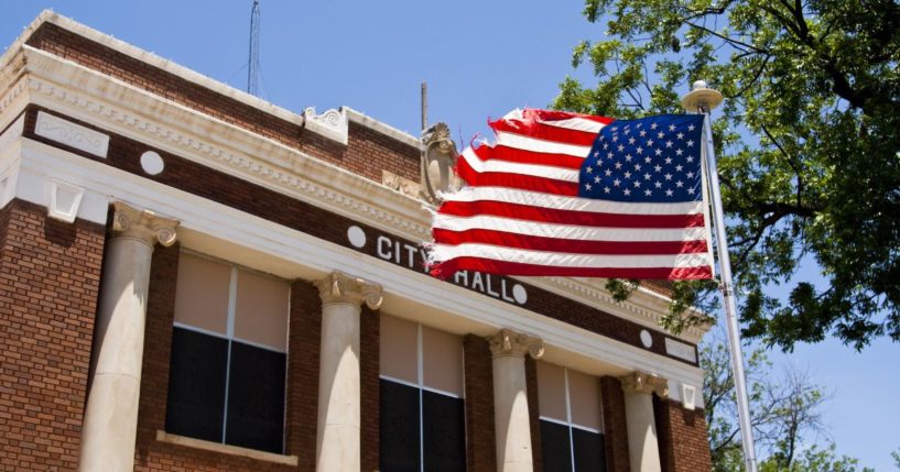 An American flag flies in front of a city hall in this stock image.