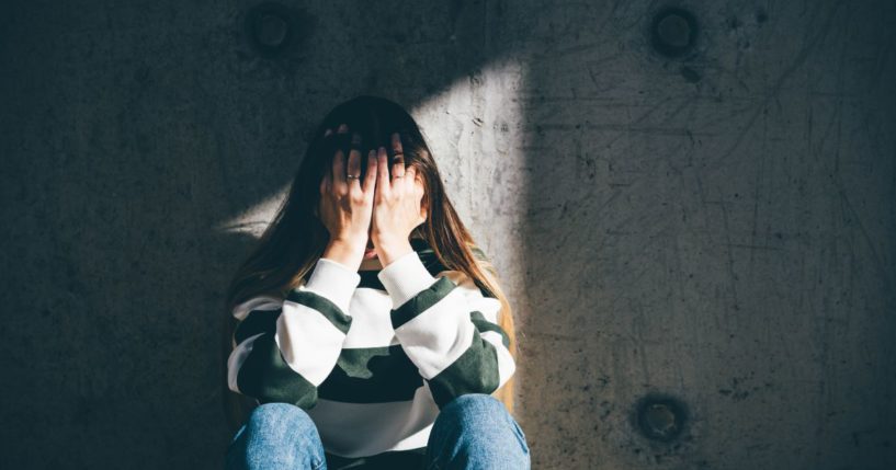 A girl sits with her head in her hands in this stock image.