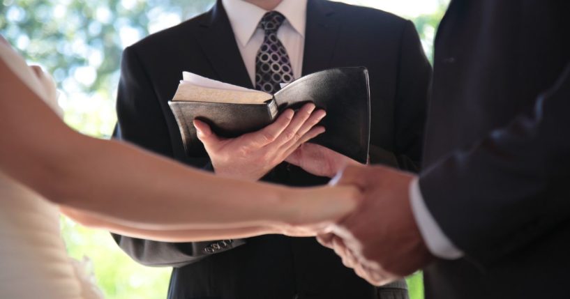 An undated stock photo shows a bride and groom holding hands in front of a pastor with a Bible during a wedding ceremony in Vancouver, British Columbia.