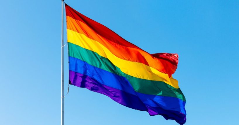 This stock image shows an LGBT flag flying on a flagpole.