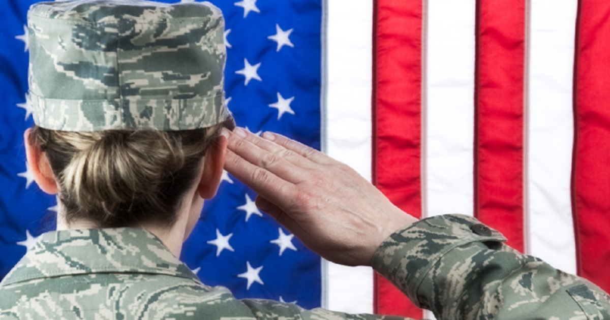 A female soldier viewed from behind saluting the American flag.