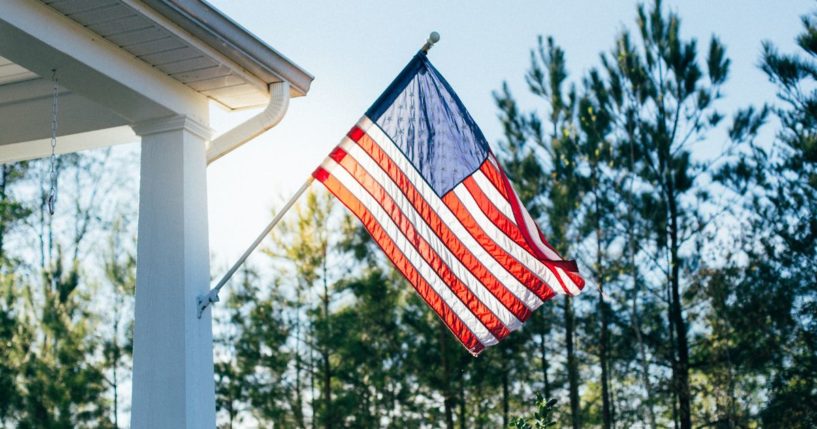 An American flag hangs from a porch in this stock image.