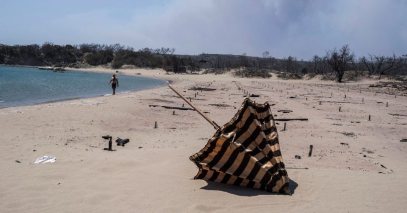 A man walks next to the burnt sunbeds and umbrellas at a beach on the Aegean Sea island of Rhodes, southeastern Greece, on Monday.