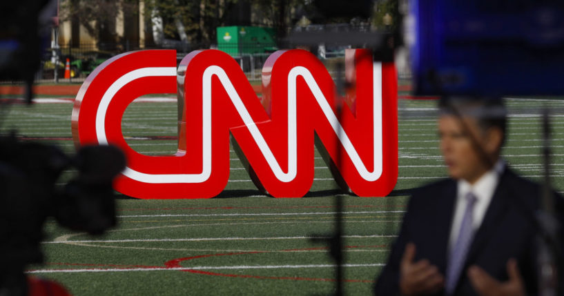 a reporter records video near a CNN sign on an athletic field