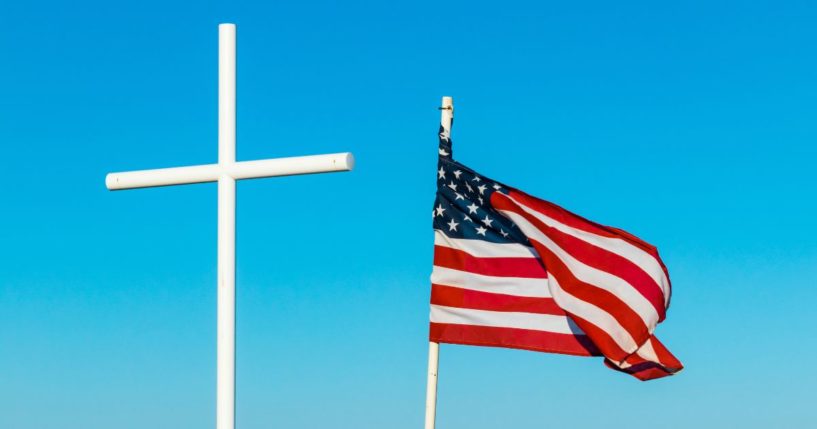 An American flag flies next to a cross in the above stock image.