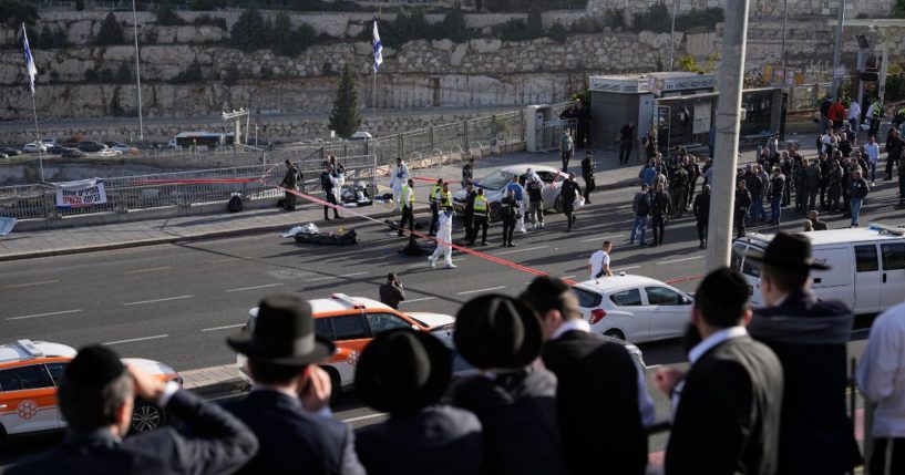 People watch as Israeli police officers and volunteers from the Zaka rescue service work the scene of a terrorist attack in Jerusalem on Thursday. Two gunman opened fire on a crowded bus station at the entrance of the city.