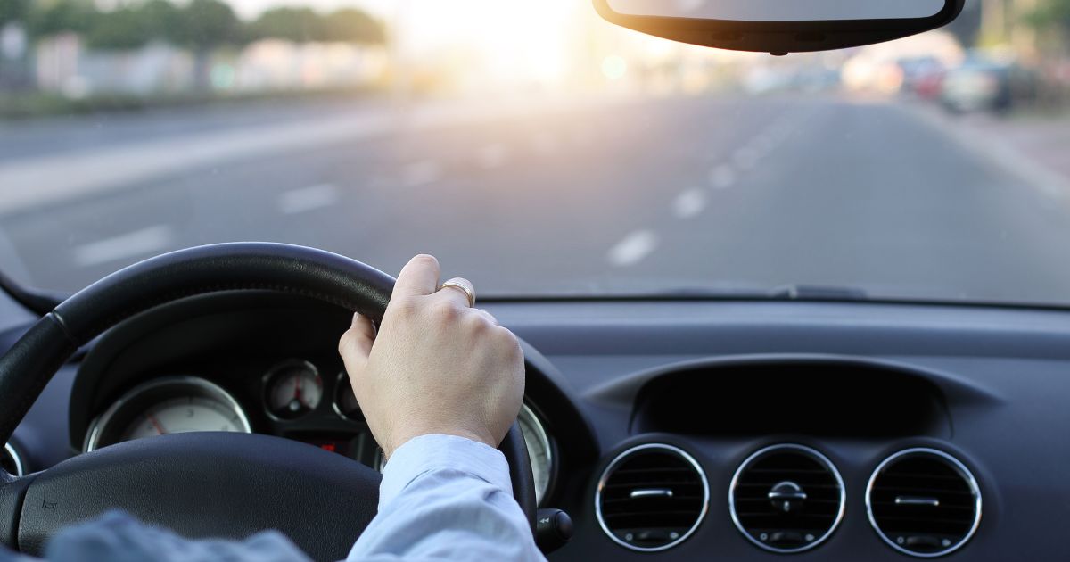 An undated stock photo shows a man's hand on a steering wheel while he drives on a sunny day.