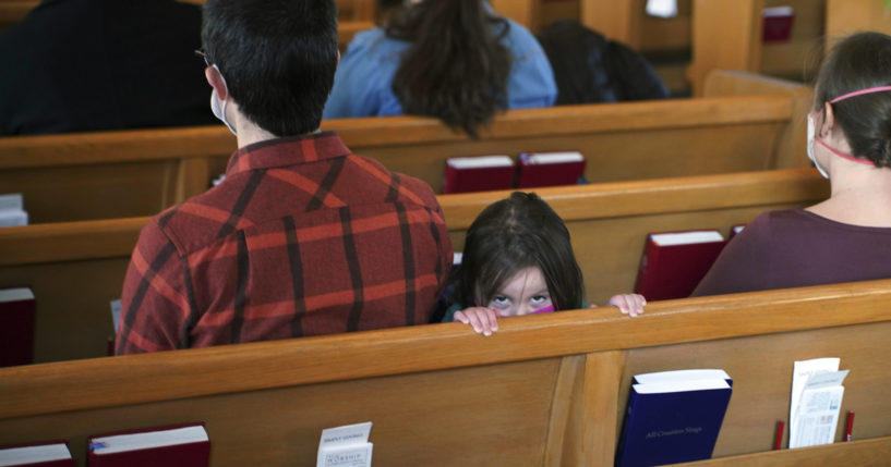 A young girl peeks above the pew next to her parents during services at Christ Church Lutheran, Jan. 23, 2022, in Minneapolis. (Jim Mone / AP)