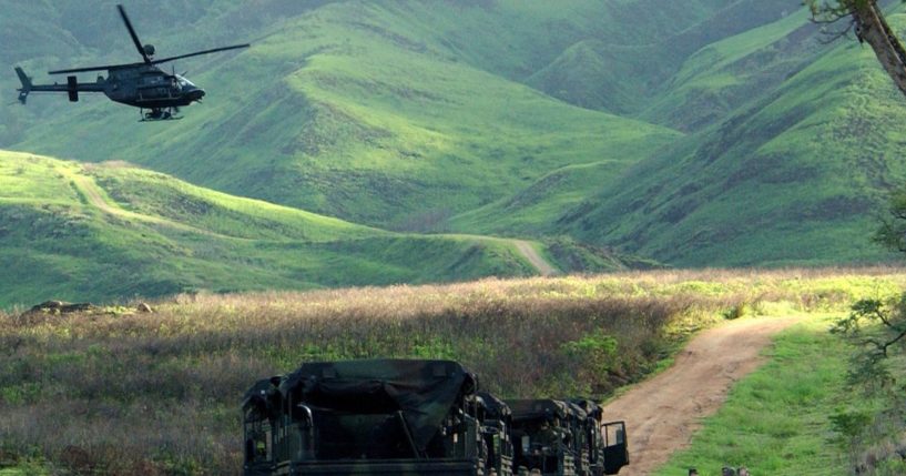 An Army Kiowa helicopter flies over a convoy of U.S. soldiers at the Makua Military Reservation in Hawaii. In a win for Native Hawaiian groups and environmentalists after decades of activism, the U.S. confirmed Friday it will permanently end live-fire training in Makua Valley on Oahu.