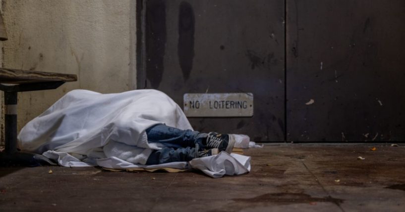 A homeless person sleeps on a dimly lit porch at the Palm School in Austin, Texas, on Monday.