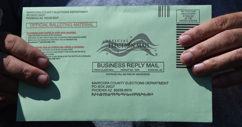 A voter displays a mail-in ballot envelope at an early voting location in Phoenix on Oct. 16, 2020.