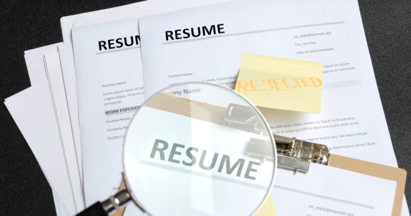 A stock photo shows resumes under a magnifying glass.