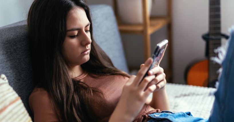 A stock photo shows a teenage girl using social media on a smartphone.