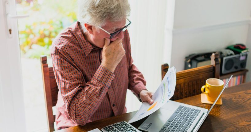 An elderly man looks at his bills in this stock image.