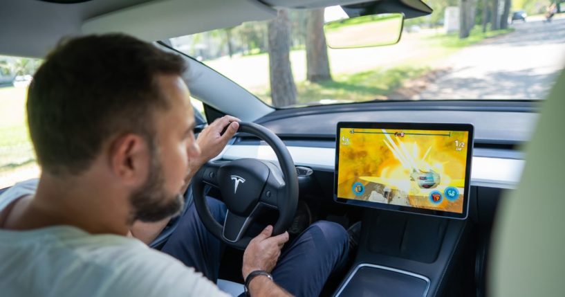 A man looks at the dashboard while driving a Tesla in this stock image.