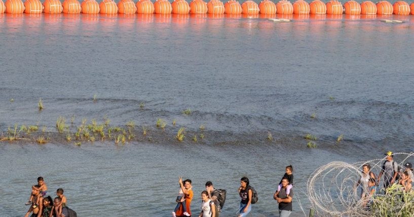 Immigrants walk by a string of buoys placed on the water along the Rio Grande border with Mexico in Eagle Pass, Texas, on July 15. The buoys are part of an operation that Texas has used to protect its borders from illegal immigration.